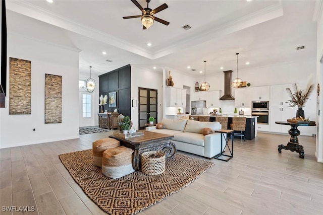 living room with ceiling fan, a raised ceiling, and ornamental molding