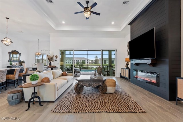 living room featuring a raised ceiling, ceiling fan, light hardwood / wood-style floors, and ornamental molding