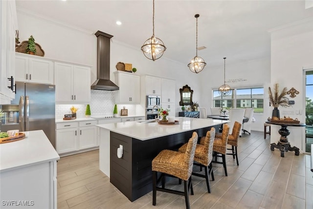 kitchen with backsplash, white cabinets, wall chimney exhaust hood, a kitchen island, and stainless steel appliances