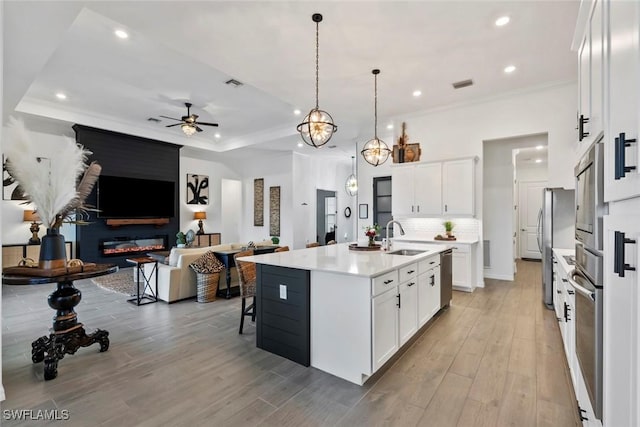 kitchen with decorative light fixtures, white cabinetry, a kitchen island with sink, and appliances with stainless steel finishes