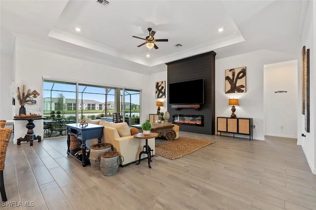 living room featuring a tray ceiling, ceiling fan, a fireplace, and ornamental molding