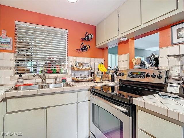 kitchen featuring stainless steel range with electric cooktop, tile counters, sink, and white cabinets