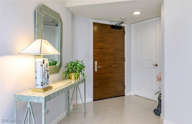 entrance foyer with light tile patterned floors, a textured ceiling, and baseboards