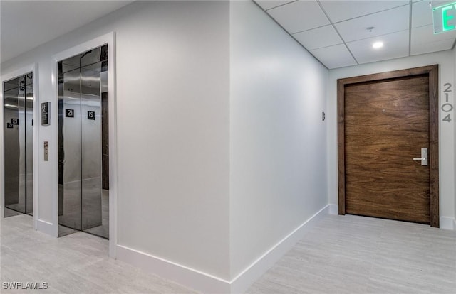 hallway with elevator, recessed lighting, a paneled ceiling, and baseboards