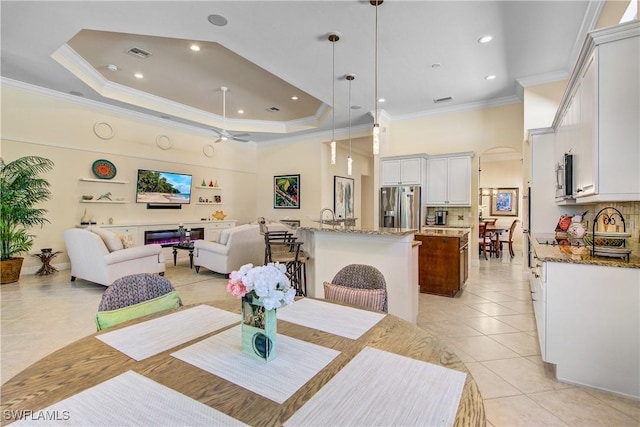 tiled dining area with ceiling fan, a raised ceiling, and ornamental molding