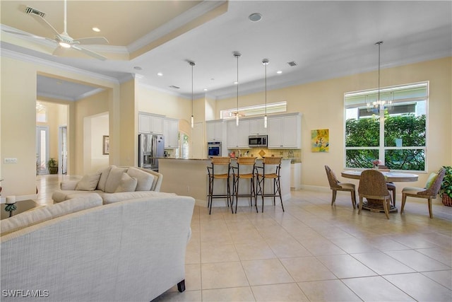 tiled living room with ceiling fan with notable chandelier, a tray ceiling, and ornamental molding