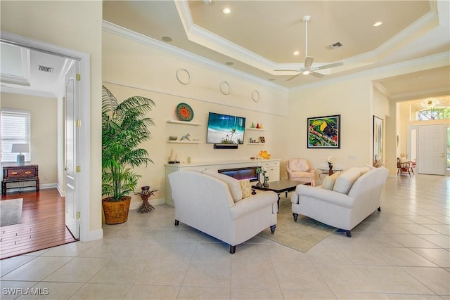 living room featuring ceiling fan, a raised ceiling, light tile patterned floors, and crown molding