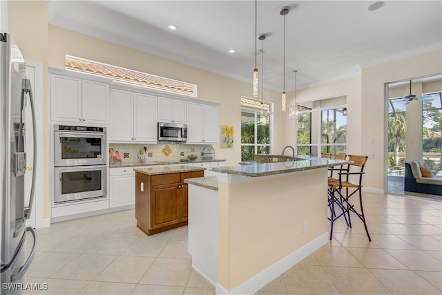 kitchen featuring white cabinetry, light stone counters, an island with sink, decorative light fixtures, and appliances with stainless steel finishes