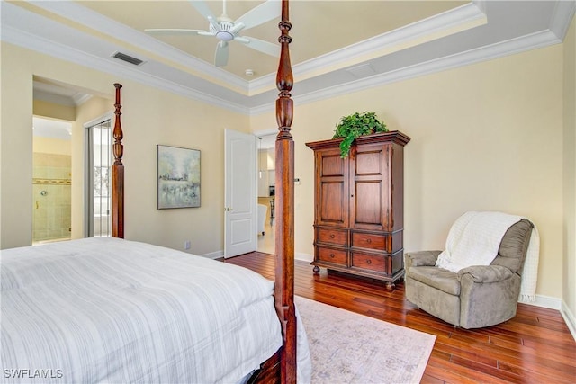 bedroom featuring a raised ceiling, crown molding, hardwood / wood-style flooring, ceiling fan, and connected bathroom