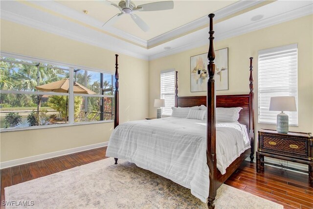 bedroom with ceiling fan, dark hardwood / wood-style floors, crown molding, and a tray ceiling