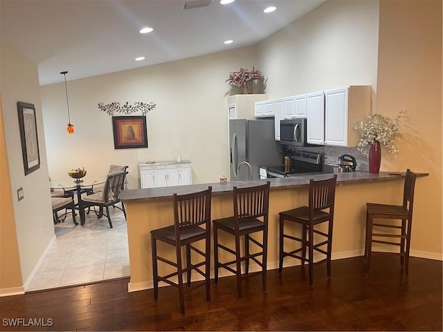 kitchen featuring white cabinets, appliances with stainless steel finishes, light hardwood / wood-style floors, a kitchen bar, and kitchen peninsula