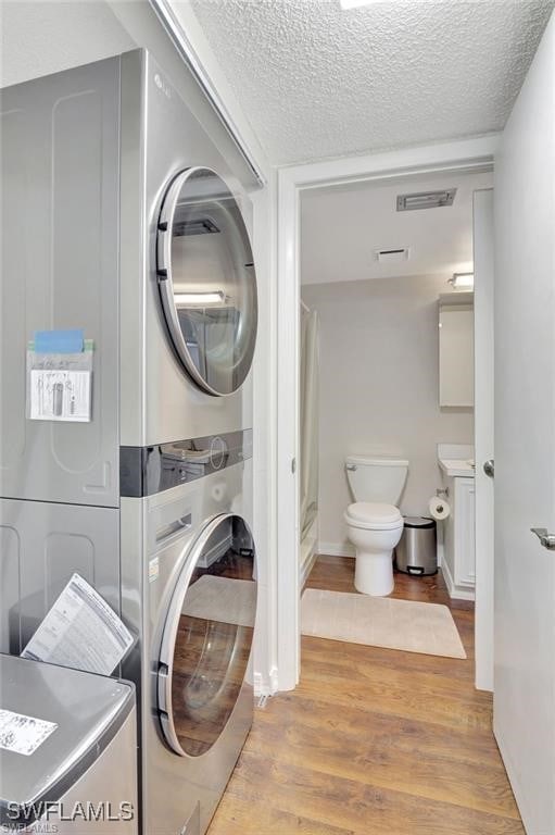 washroom featuring a textured ceiling, light wood-type flooring, and stacked washer / dryer