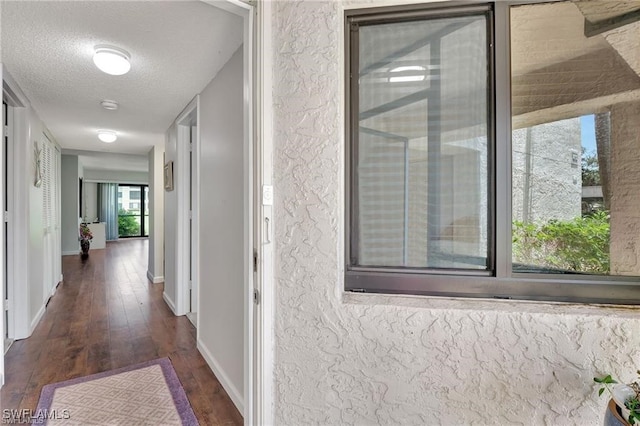 corridor with dark wood finished floors, a textured ceiling, and baseboards