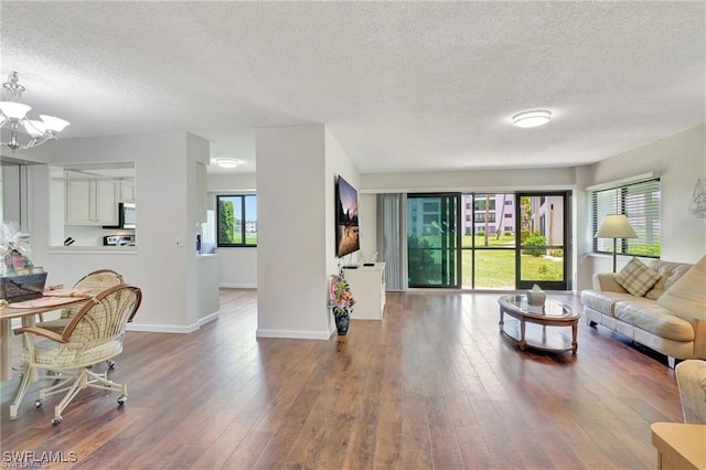 living room with baseboards, a textured ceiling, hardwood / wood-style flooring, and a notable chandelier