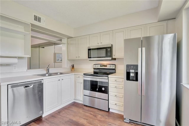 kitchen featuring appliances with stainless steel finishes, a textured ceiling, sink, hardwood / wood-style flooring, and white cabinets