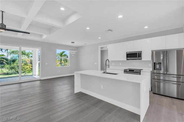 kitchen with coffered ceiling, a center island with sink, sink, appliances with stainless steel finishes, and white cabinetry