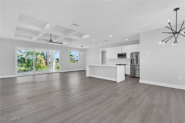 unfurnished living room with sink, coffered ceiling, beamed ceiling, hardwood / wood-style floors, and ceiling fan with notable chandelier