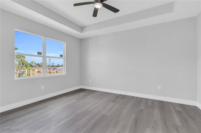 unfurnished room with hardwood / wood-style floors, ceiling fan, and a raised ceiling