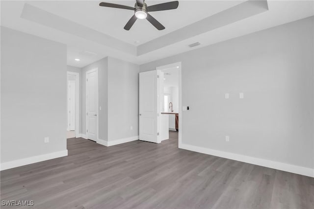 unfurnished room with hardwood / wood-style flooring, ceiling fan, sink, and a tray ceiling