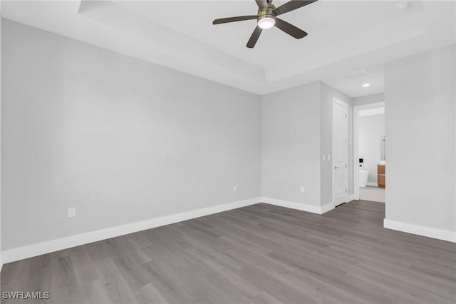 unfurnished room featuring dark hardwood / wood-style flooring, a tray ceiling, and ceiling fan