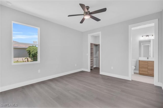 unfurnished bedroom featuring ensuite bathroom, a spacious closet, ceiling fan, and light hardwood / wood-style flooring