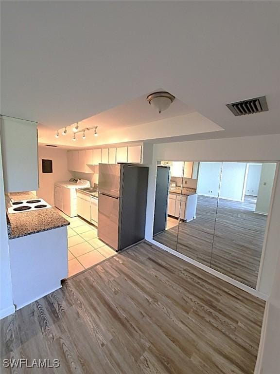 kitchen featuring white cabinetry, stainless steel fridge, washing machine and clothes dryer, dark stone counters, and light hardwood / wood-style flooring