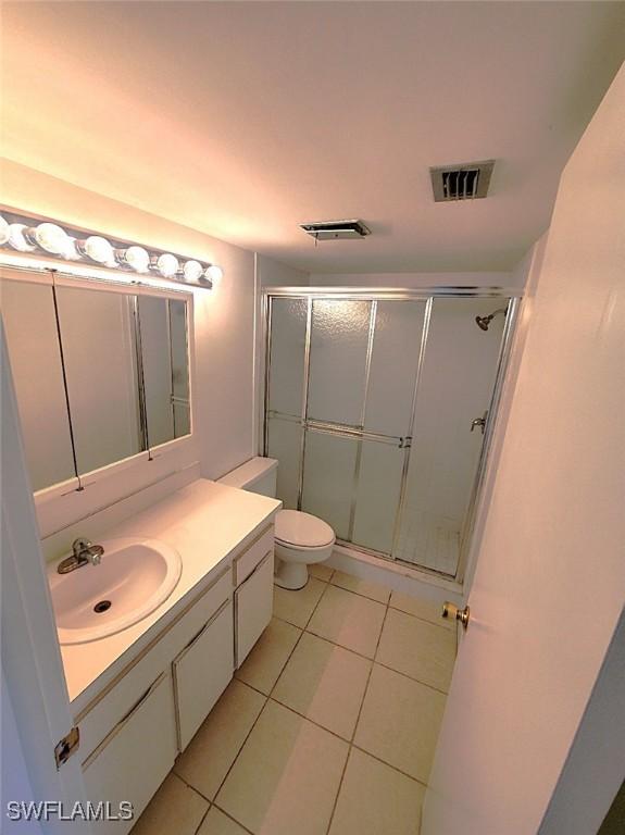 bathroom with a shower with shower door, vanity, tile patterned floors, and toilet