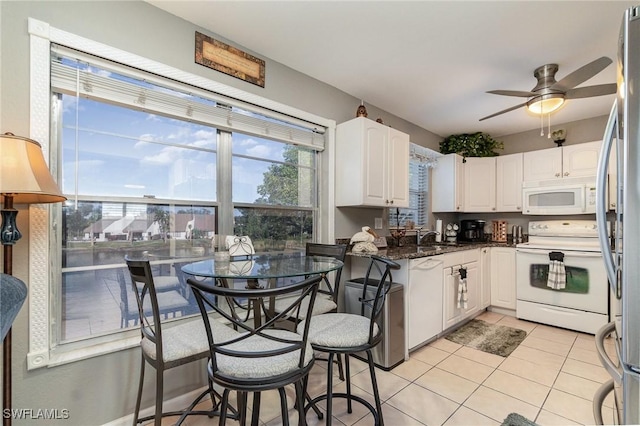 kitchen with white appliances, white cabinets, ceiling fan, light tile patterned flooring, and dark stone counters