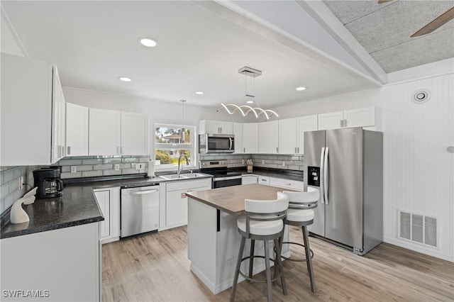 kitchen featuring a center island, sink, decorative light fixtures, white cabinetry, and stainless steel appliances