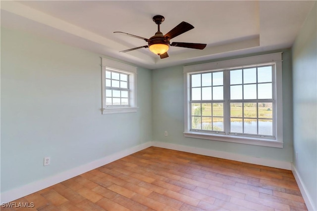 spare room with ceiling fan, light hardwood / wood-style floors, and a tray ceiling