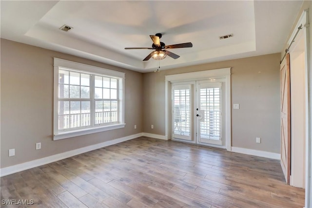 unfurnished room with a barn door, light hardwood / wood-style floors, a raised ceiling, and ceiling fan