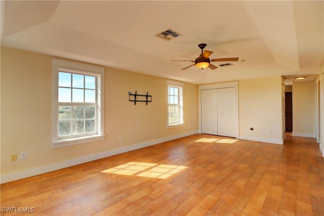 unfurnished bedroom featuring ceiling fan, light hardwood / wood-style floors, multiple windows, and a closet