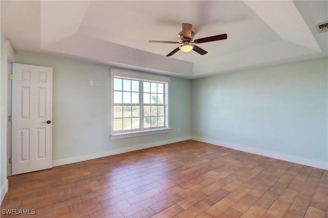 unfurnished room with light wood-type flooring, a tray ceiling, and ceiling fan