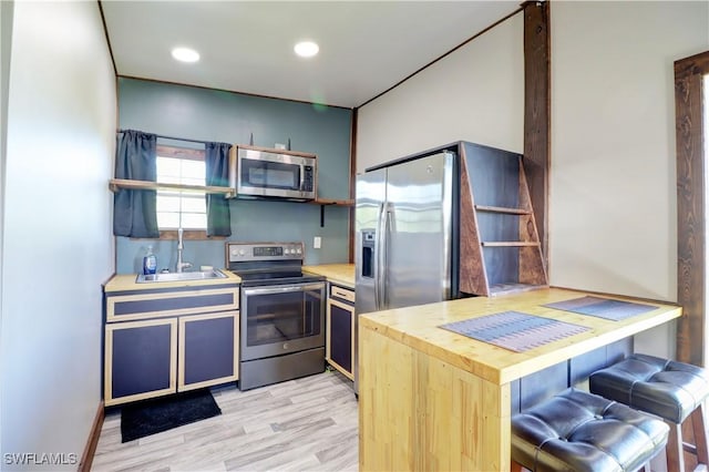 kitchen featuring sink, stainless steel appliances, kitchen peninsula, a kitchen bar, and light wood-type flooring