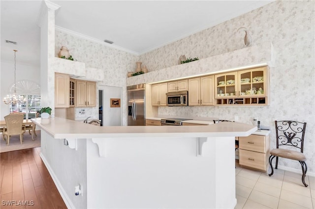 kitchen featuring kitchen peninsula, ornamental molding, stainless steel appliances, a chandelier, and a breakfast bar area