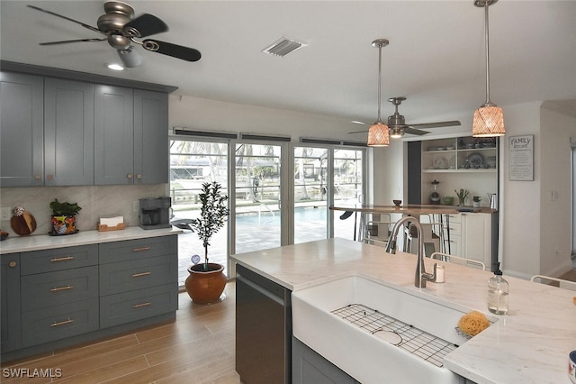 kitchen featuring light wood-type flooring, light stone counters, gray cabinetry, sink, and hanging light fixtures