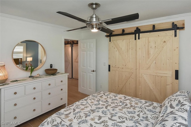 bedroom featuring a barn door, crown molding, ceiling fan, and dark hardwood / wood-style floors