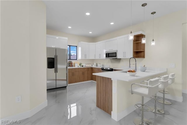 kitchen with kitchen peninsula, appliances with stainless steel finishes, decorative light fixtures, white cabinetry, and a breakfast bar area