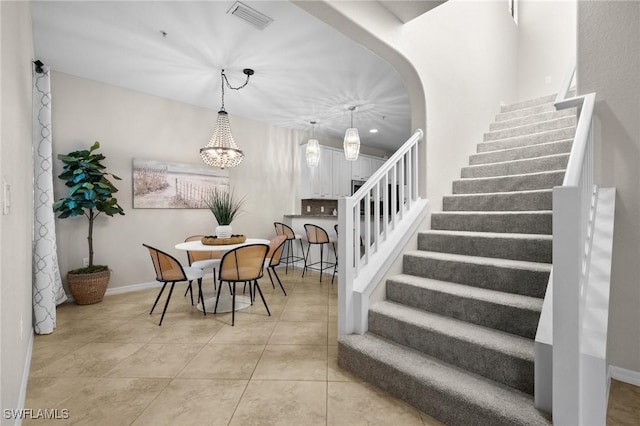 stairs with tile patterned floors and a notable chandelier