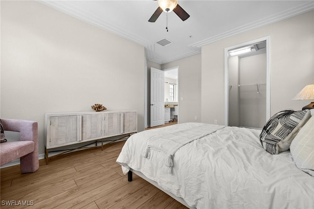 bedroom with a walk in closet, ornamental molding, ceiling fan, light hardwood / wood-style floors, and a closet