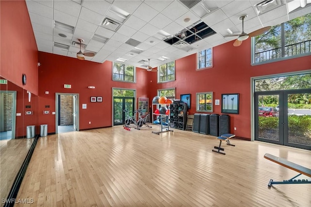 workout area featuring hardwood / wood-style flooring, ceiling fan, a drop ceiling, and a towering ceiling