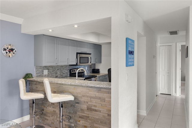 kitchen with a kitchen bar, appliances with stainless steel finishes, backsplash, light stone counters, and gray cabinetry