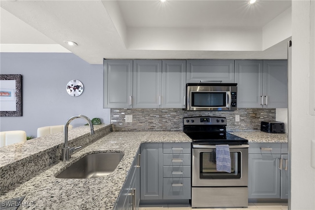 kitchen featuring sink, gray cabinets, light stone countertops, tasteful backsplash, and stainless steel appliances