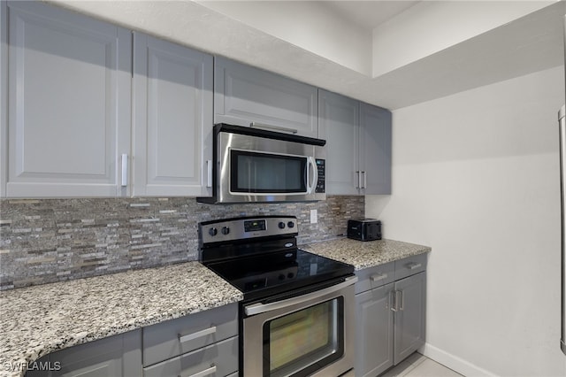 kitchen with gray cabinetry, decorative backsplash, light stone countertops, light tile patterned floors, and stainless steel appliances