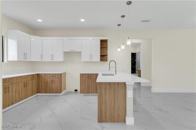 kitchen featuring kitchen peninsula, decorative light fixtures, white cabinetry, and sink