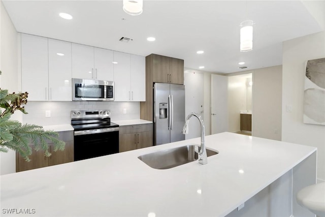 kitchen with pendant lighting, white cabinets, sink, decorative backsplash, and appliances with stainless steel finishes