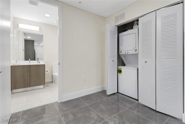 laundry area featuring tile patterned flooring, sink, and stacked washer and clothes dryer