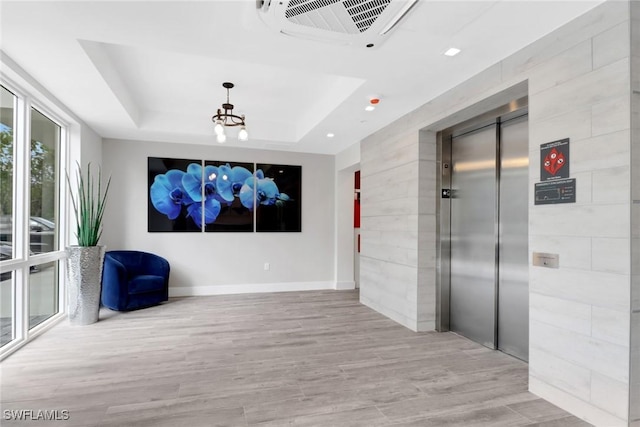 cinema room with a raised ceiling, elevator, and light hardwood / wood-style floors