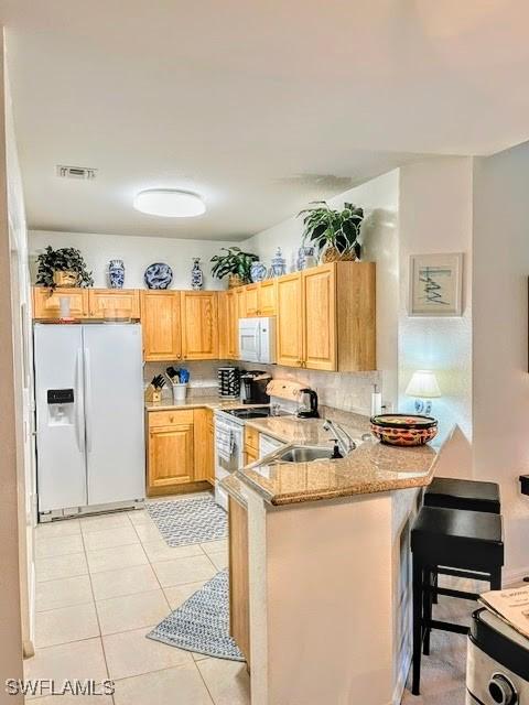 kitchen featuring kitchen peninsula, a kitchen bar, white appliances, sink, and light tile patterned floors