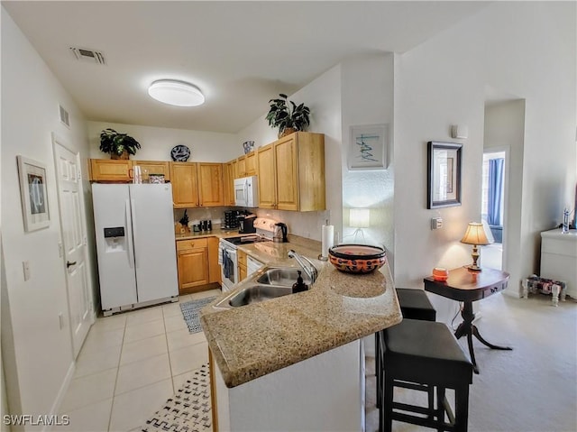 kitchen featuring sink, kitchen peninsula, white appliances, a breakfast bar, and light tile patterned floors